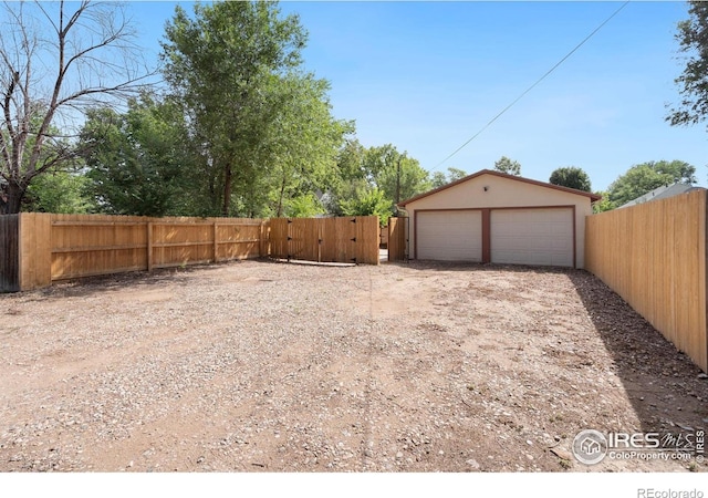 view of yard featuring a gate, a detached garage, an outbuilding, and fence