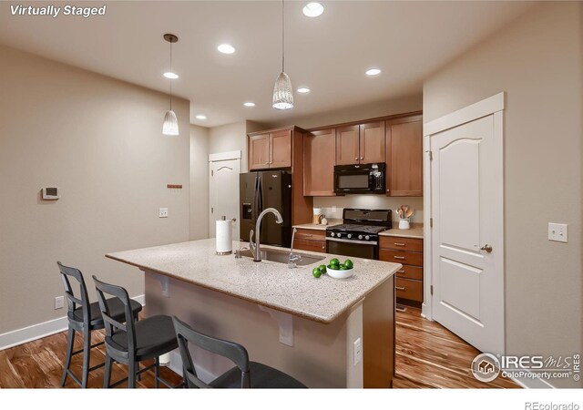 8482 Parkland St, Broomfield, CO 80021 - kitchen featuring black appliances, wood finished floors, a sink, a kitchen breakfast bar, and a kitchen island with sink