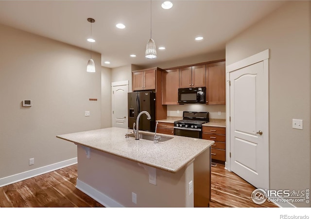 8482 Parkland St, Broomfield, CO 80021 - kitchen with black appliances, wood finished floors, a sink, a center island with sink, and baseboards