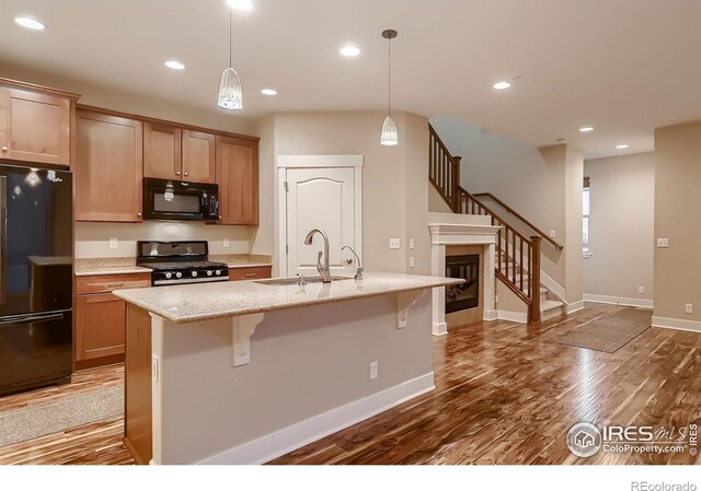 8482 Parkland St, Broomfield, CO 80021 - kitchen featuring black appliances, a sink, wood finished floors, a kitchen breakfast bar, and an island with sink