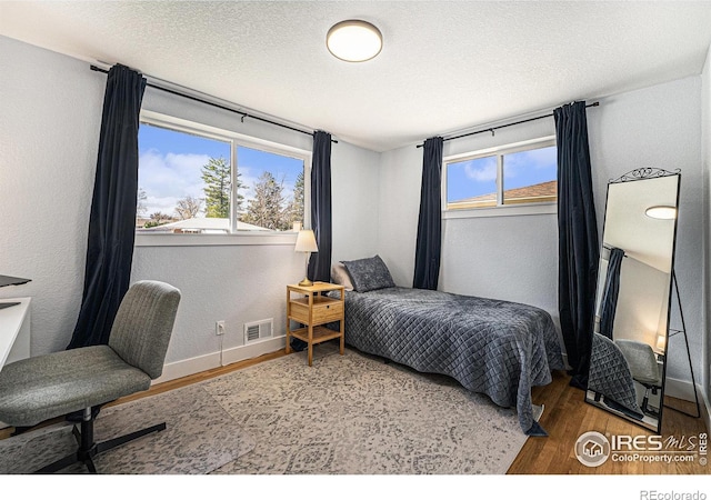 2566 S Stuart St, Denver, CO 80219 - bedroom featuring wood finished floors, multiple windows, baseboards, a textured wall, and a textured ceiling