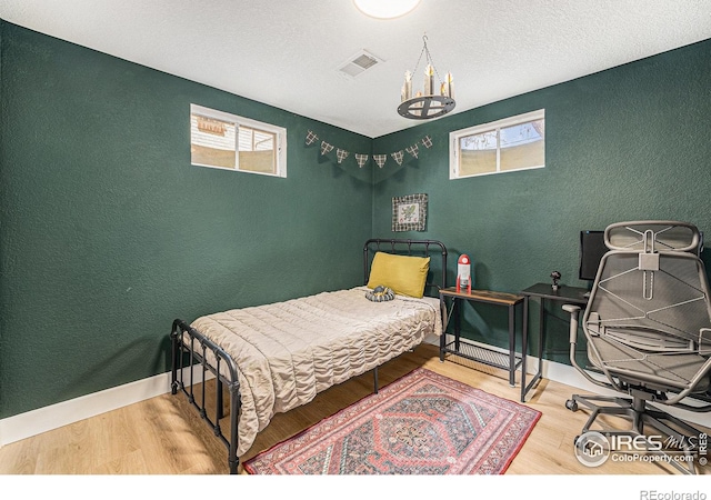 2566 S Stuart St, Denver, CO 80219 - bedroom featuring a textured wall, multiple windows, wood finished floors, a chandelier, and baseboards