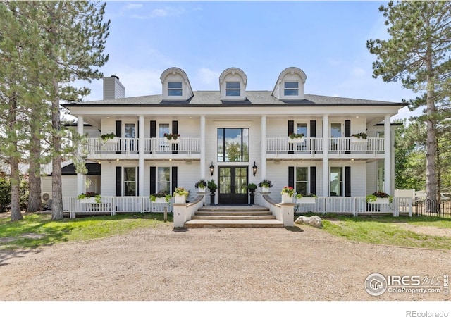 view of front of home with french doors, covered porch, a balcony, and a chimney