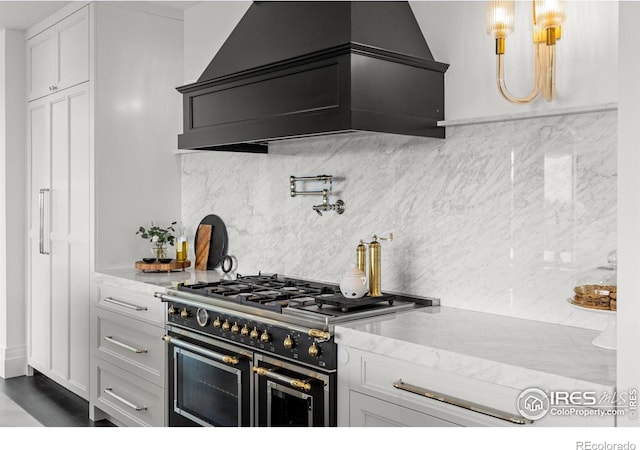 kitchen featuring range with two ovens, decorative backsplash, white cabinetry, and premium range hood