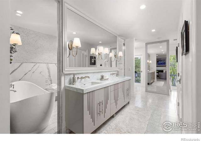 bathroom with recessed lighting, a freestanding bath, double vanity, a chandelier, and a fireplace