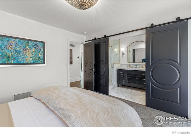 bedroom with a barn door, ensuite bathroom, and baseboards