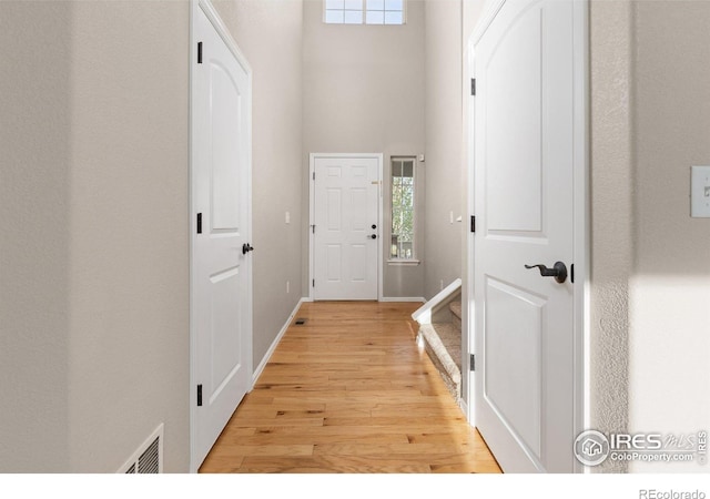 doorway to outside featuring baseboards, visible vents, light wood-style flooring, and a towering ceiling