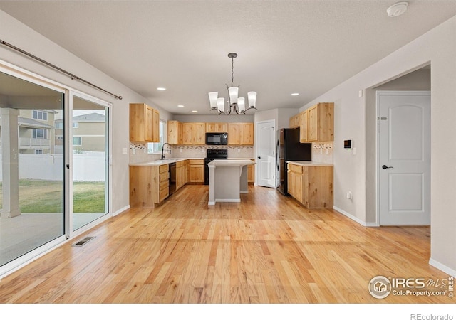 kitchen with light countertops, black appliances, light wood-style flooring, and a notable chandelier