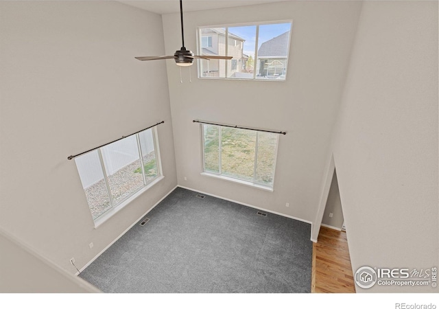 interior space with visible vents, a towering ceiling, baseboards, a ceiling fan, and carpet