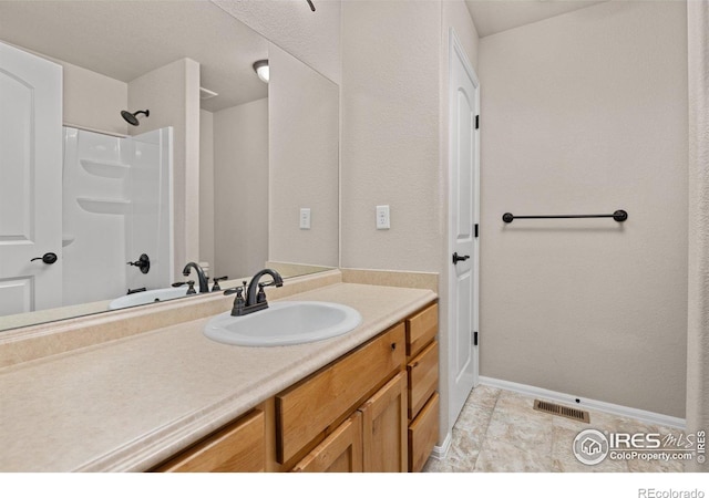 full bathroom with baseboards, vanity, a shower, and visible vents