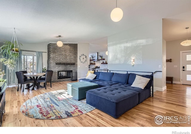 living area with baseboards, a brick fireplace, and wood finished floors