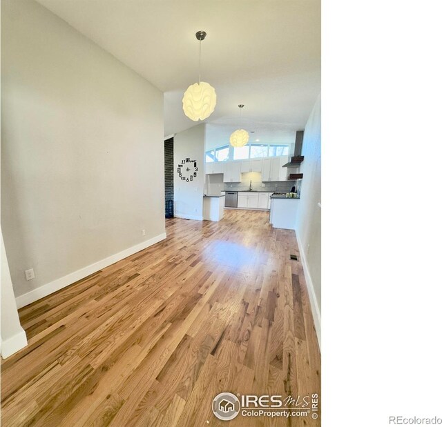 unfurnished dining area with visible vents, vaulted ceiling, a sink, baseboards, and light wood-style floors