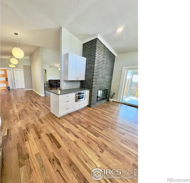 unfurnished living room with light wood-type flooring, a textured ceiling, baseboards, and a large fireplace