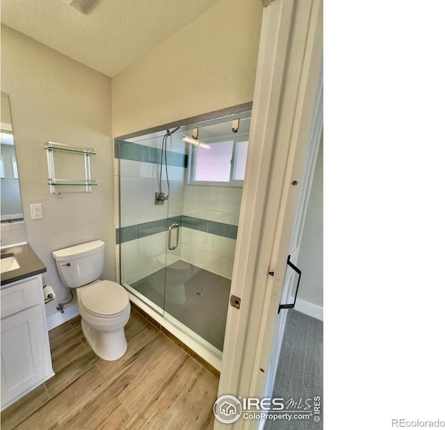 bathroom featuring vanity, wood finished floors, toilet, a textured ceiling, and a stall shower