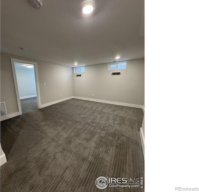 basement featuring dark carpet, a textured ceiling, and baseboards