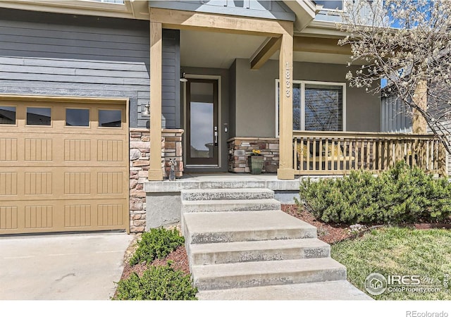 doorway to property with stucco siding, a garage, stone siding, and covered porch