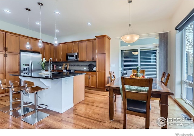 kitchen with stainless steel appliances, tasteful backsplash, dark countertops, light wood-style floors, and brown cabinets