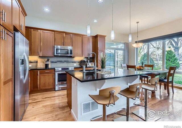 kitchen with stainless steel appliances, light wood-style flooring, a sink, dark countertops, and a breakfast bar area