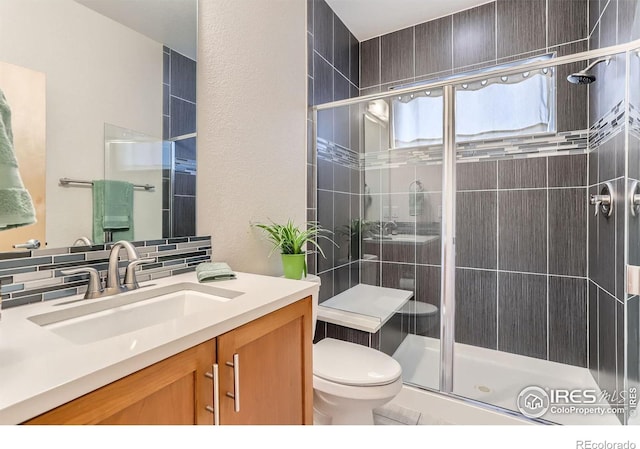 full bath with a textured wall, vanity, toilet, and a stall shower
