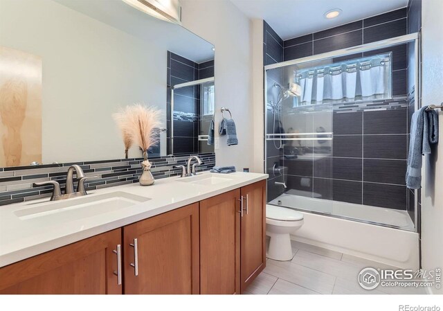 full bath with shower / bath combination with glass door, a sink, double vanity, and tasteful backsplash