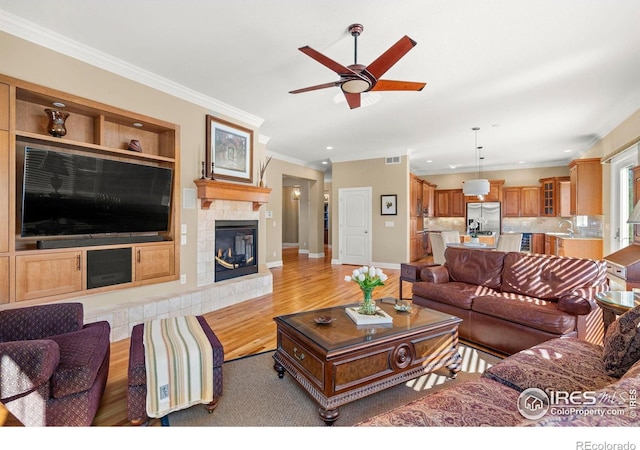 living area featuring a ceiling fan, crown molding, visible vents, and light wood-type flooring