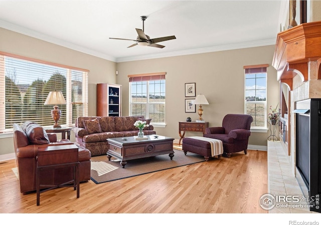 living room with crown molding, a fireplace with raised hearth, ceiling fan, light wood-style flooring, and baseboards