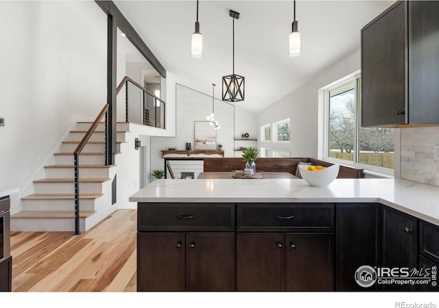 kitchen with a peninsula, light wood-style floors, lofted ceiling, light countertops, and decorative light fixtures