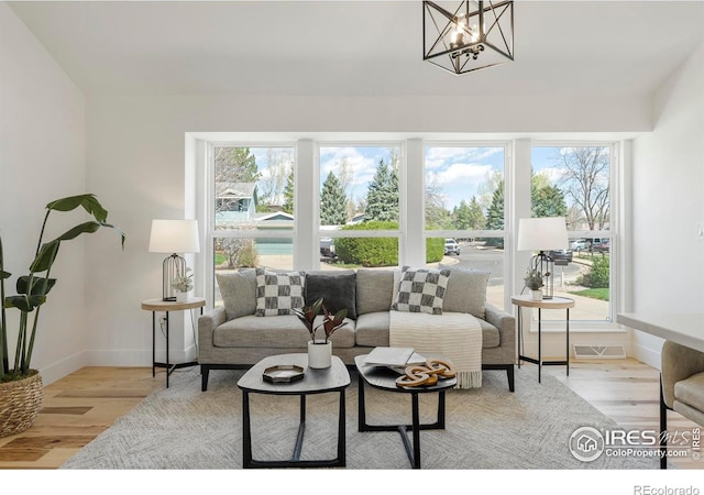 living area with light wood-type flooring, an inviting chandelier, visible vents, and baseboards
