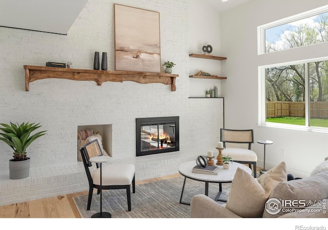sitting room with wood finished floors, a brick fireplace, and a high ceiling