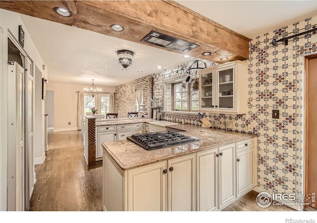 3707 Shelter Cv, Fort Collins, CO 80525 - kitchen with a peninsula, cooktop, wood finished floors, a chandelier, and glass insert cabinets