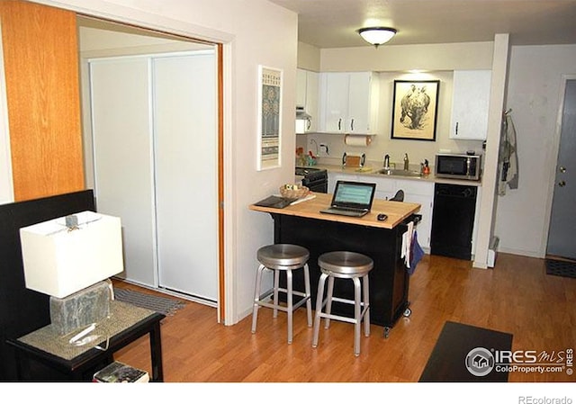 kitchen featuring light wood-style floors, light countertops, white cabinets, a sink, and black appliances