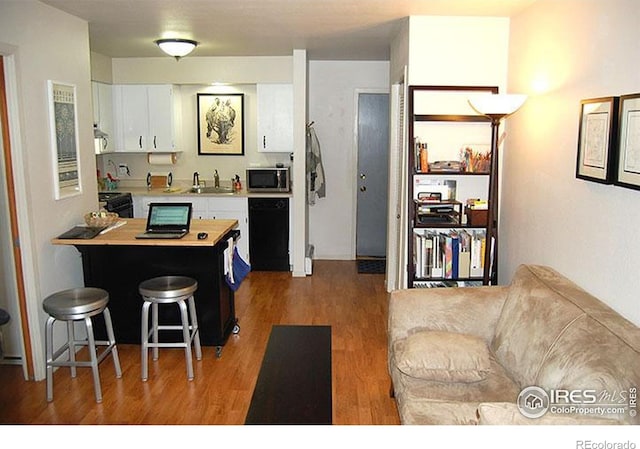 kitchen with white cabinets, a sink, light countertops, stainless steel microwave, and wood finished floors