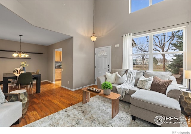 living area featuring hardwood / wood-style floors, baseboards, a high ceiling, and a notable chandelier