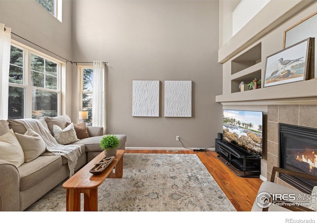 living area with a tile fireplace, a high ceiling, wood finished floors, and baseboards