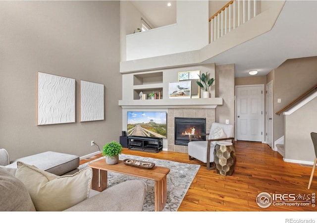 living room featuring baseboards, built in features, a high ceiling, hardwood / wood-style floors, and a tile fireplace