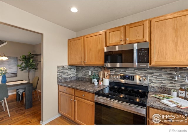 kitchen featuring light wood finished floors, dark countertops, baseboards, decorative backsplash, and appliances with stainless steel finishes