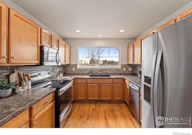 kitchen with a sink, dark countertops, stainless steel appliances, and light wood-style flooring