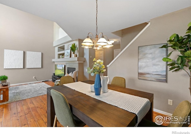 dining area with a fireplace, baseboards, an inviting chandelier, and light wood-style floors