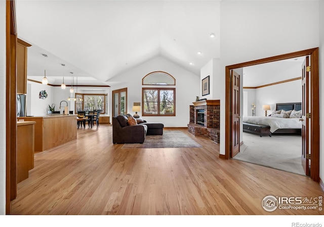 living area with high vaulted ceiling, a brick fireplace, and light wood-style flooring