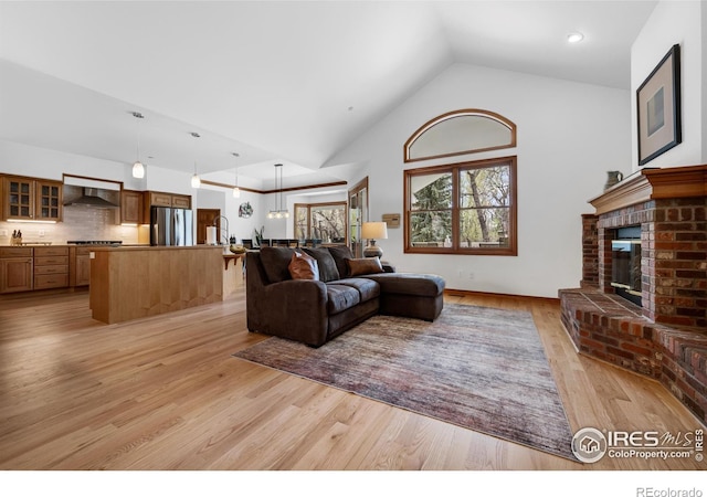 living room with light wood-type flooring, high vaulted ceiling, and a fireplace