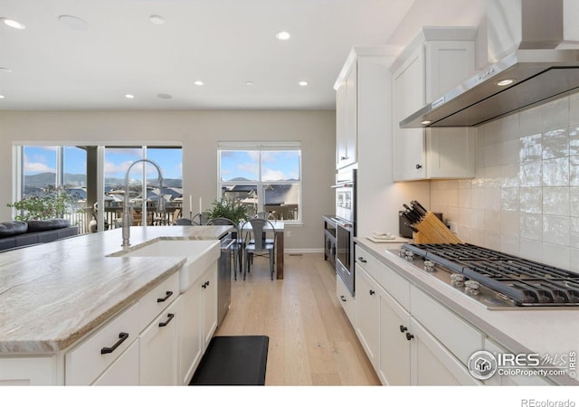 3351 Heron Lakes Pkwy, Berthoud, CO 80513 - kitchen with light wood finished floors, wall chimney range hood, a sink, decorative backsplash, and appliances with stainless steel finishes