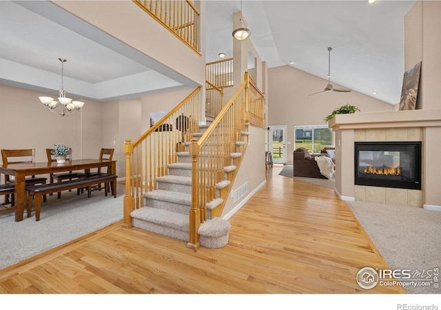 stairs featuring a tiled fireplace, ceiling fan with notable chandelier, wood finished floors, and visible vents