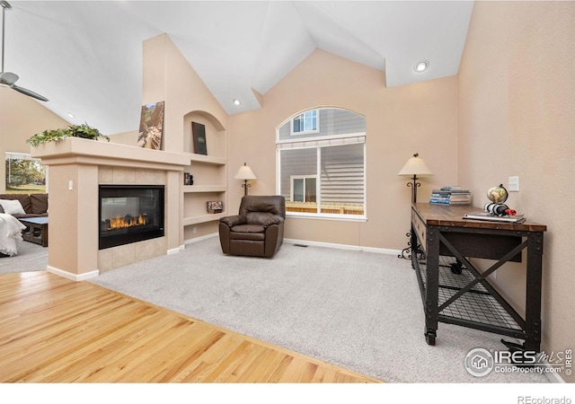 living area with wood finished floors, baseboards, high vaulted ceiling, built in shelves, and a tile fireplace