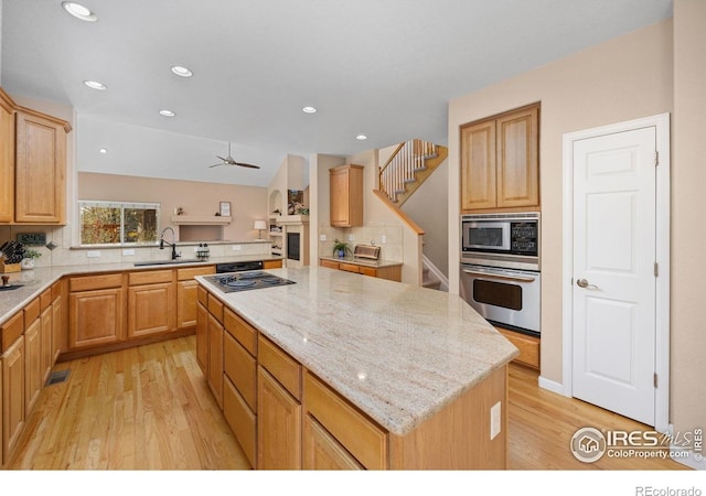 kitchen featuring appliances with stainless steel finishes, a sink, a center island, light wood-type flooring, and backsplash