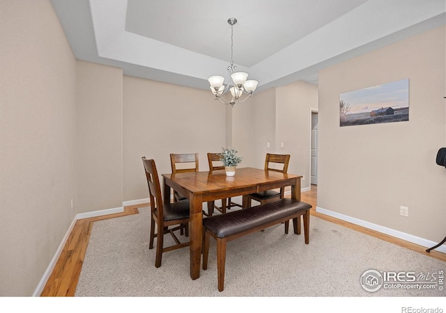 dining area featuring baseboards, a tray ceiling, wood finished floors, and a notable chandelier