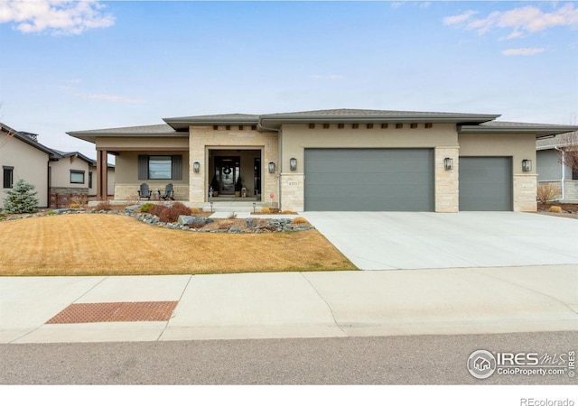 prairie-style home with stucco siding, driveway, stone siding, a front yard, and a garage