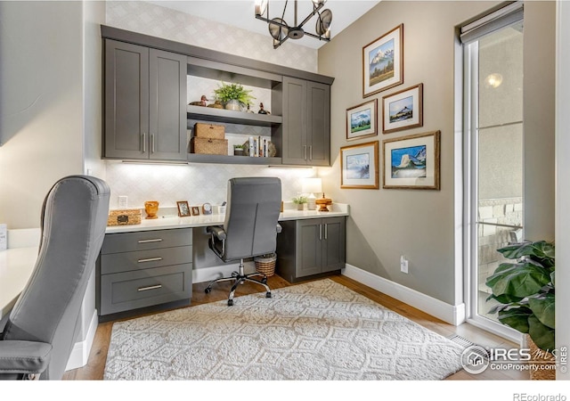 office area featuring baseboards, a chandelier, light wood finished floors, and built in desk