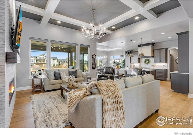 living room with light wood-style flooring, an inviting chandelier, coffered ceiling, and a fireplace
