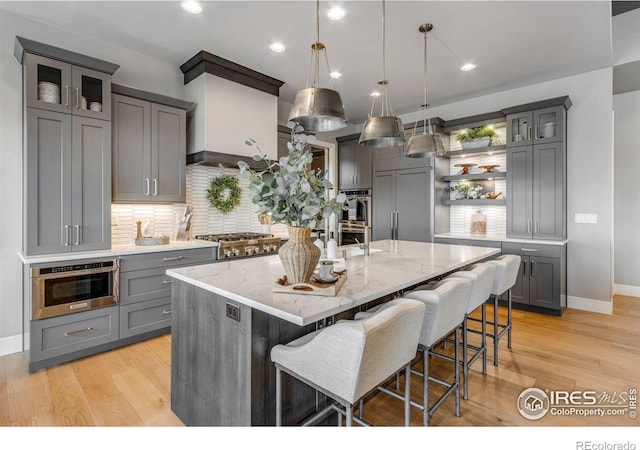 kitchen with gray cabinets, built in refrigerator, a center island with sink, decorative backsplash, and a kitchen bar