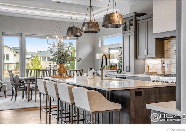 kitchen with wood finished floors, glass insert cabinets, a kitchen bar, backsplash, and decorative light fixtures